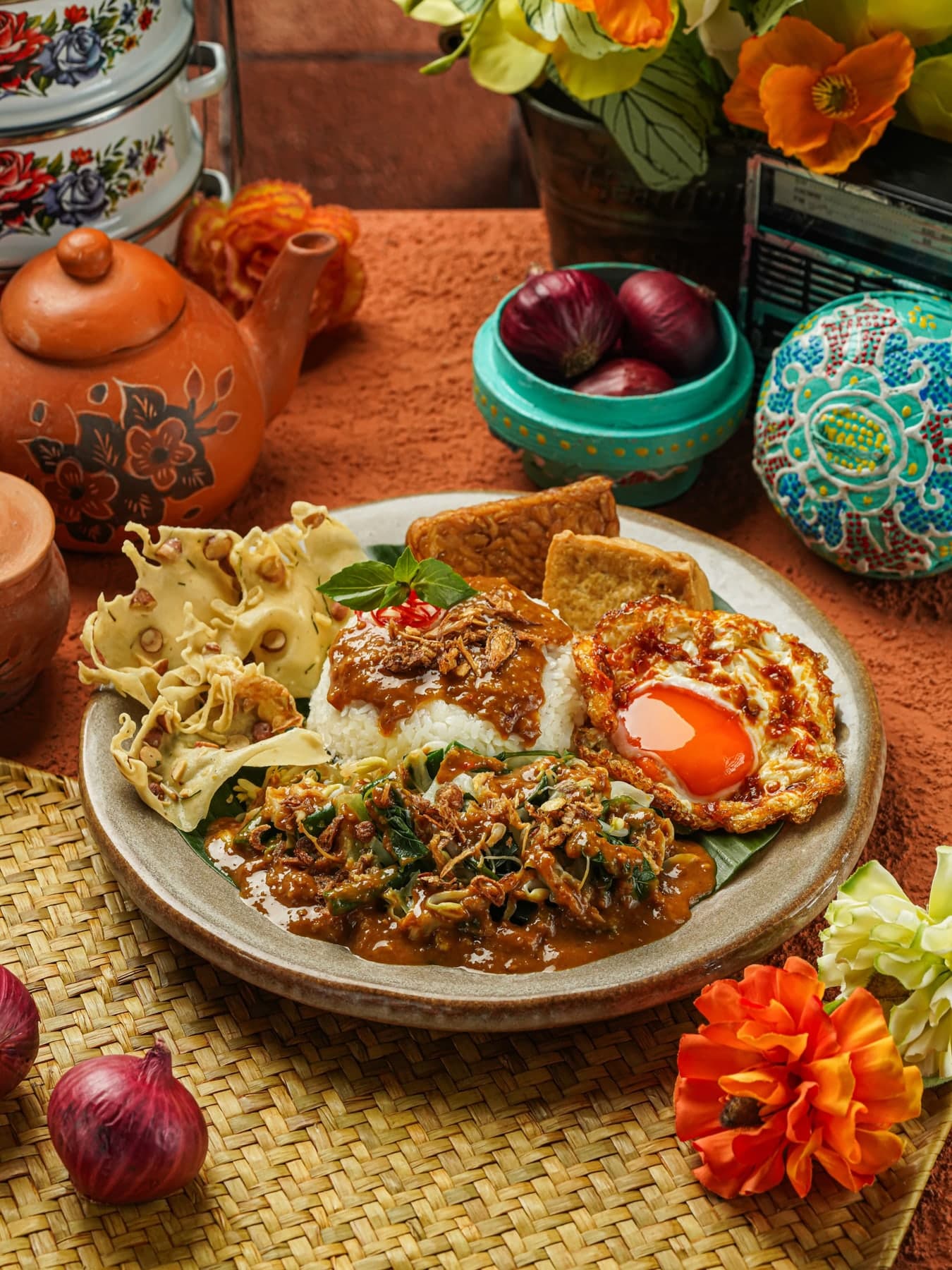 A plate of nasi pecel: rice, blanched vegetables, peanut sauce, a fried egg and crackers, on a patterned tablecloth